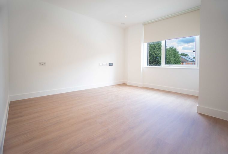 A spacious, unfurnished room with white walls, wood-effect flooring, and a large window.