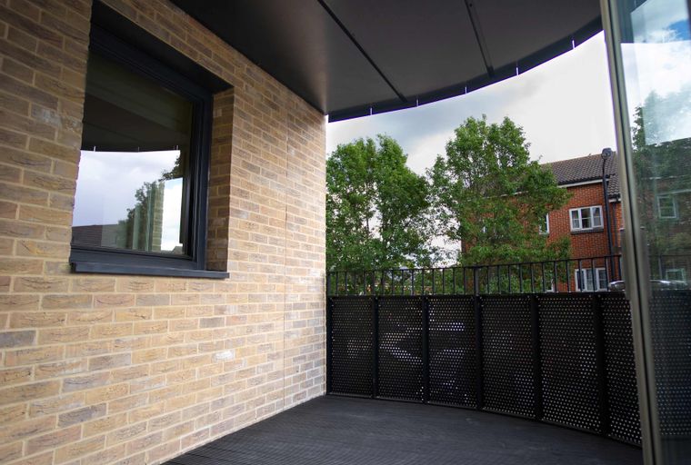 A balcony with a brick wall, black decking, and a perforated metal screen.