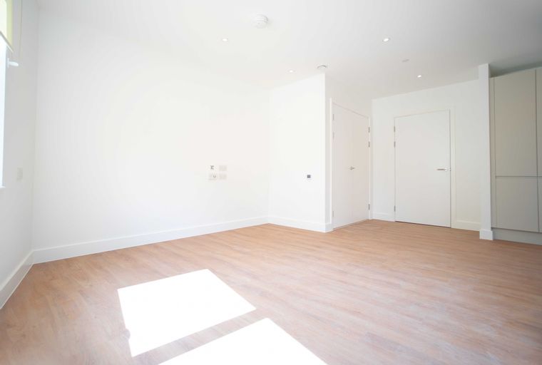 A spacious, unfurnished room with light wood laminate flooring and white walls.