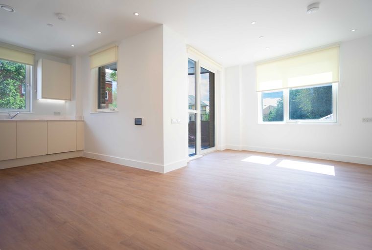 An empty room with a kitchen area, large windows, and wood-effect flooring.