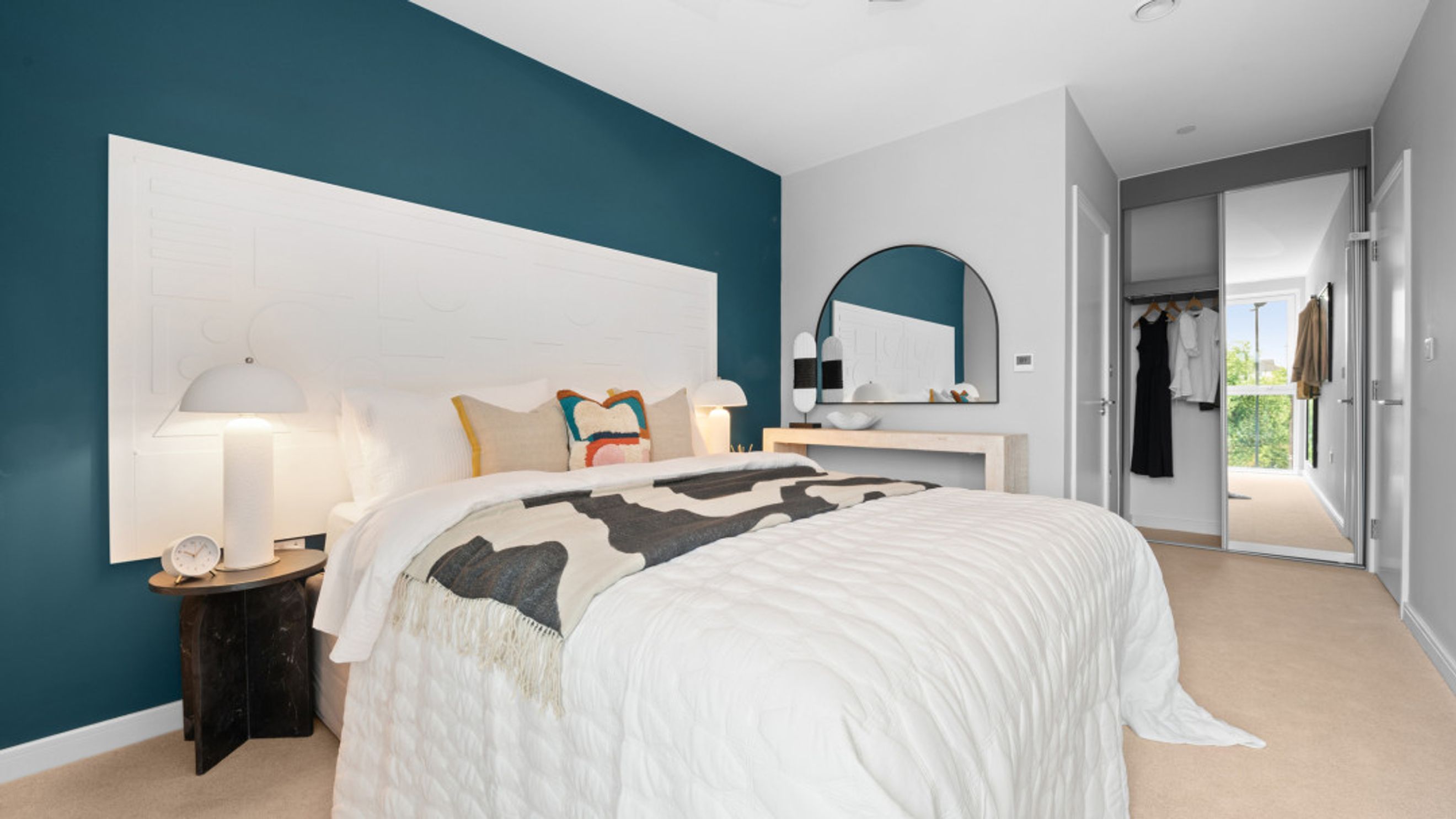 A bedroom with a bed, bedside table, lamp, and mirrored wardrobe.