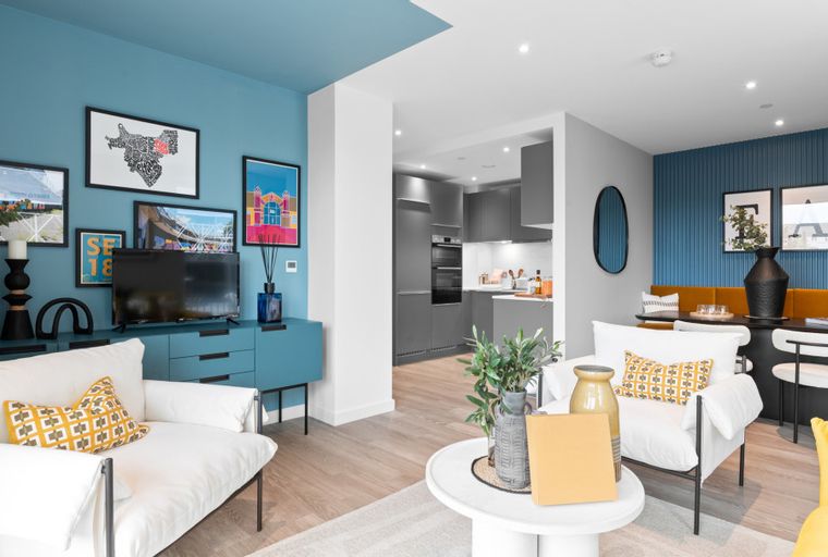 A living room and kitchen area with white sofas, a blue wall, and grey cabinets.