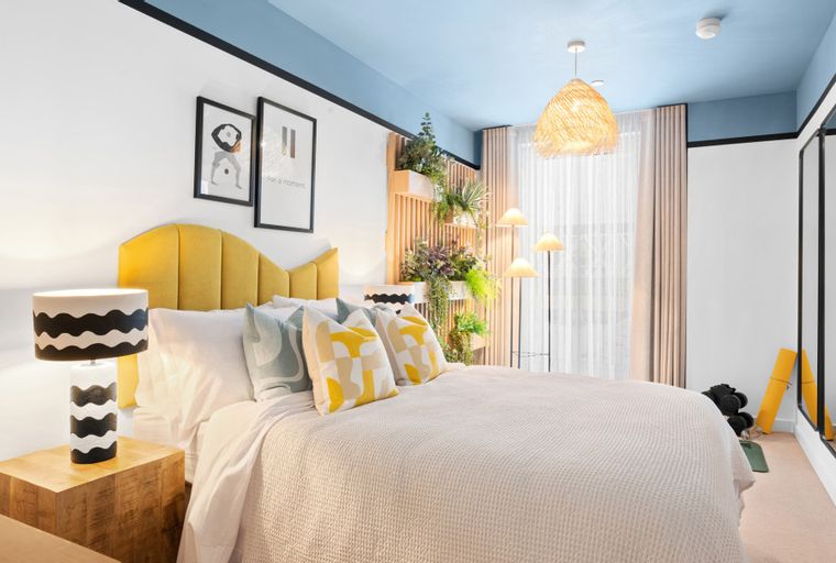 A bedroom with a bed, pillows, lamps, and artwork.