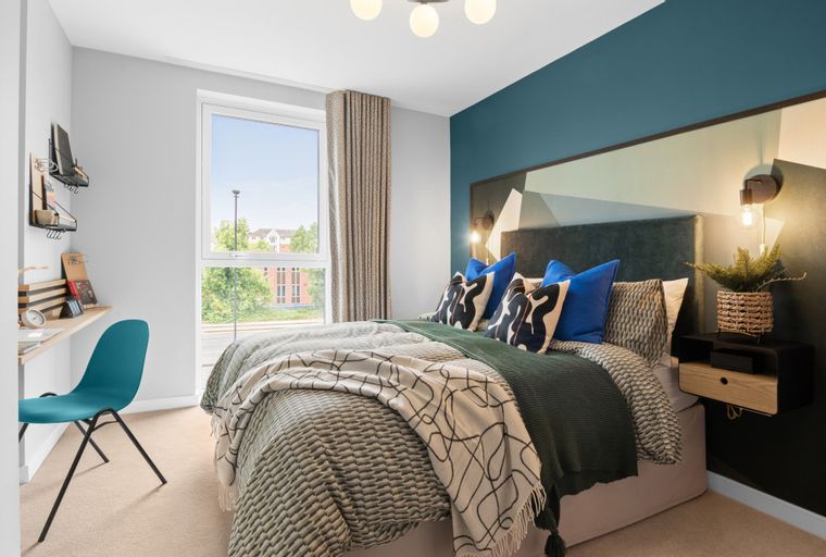 A bedroom with a bed, pillows, a desk, and a chair.