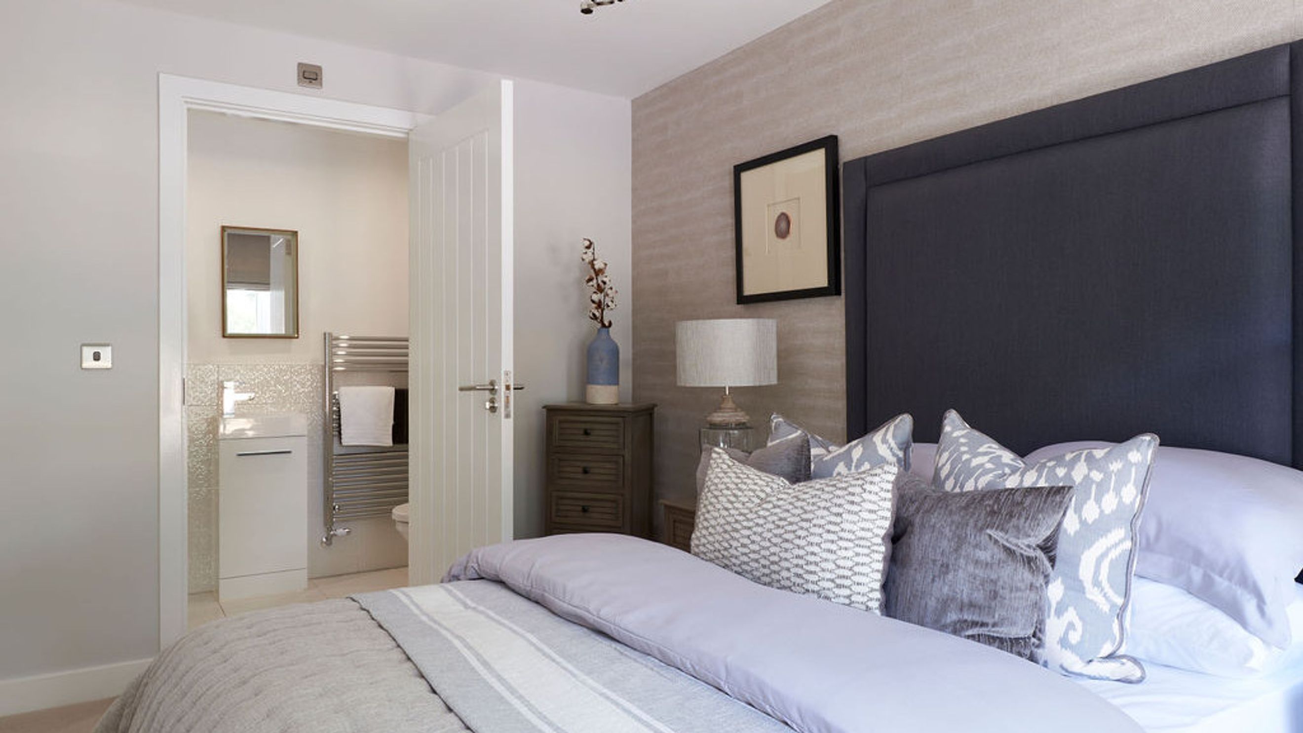 A bedroom with a bed, pillows, a headboard, and an en-suite bathroom.