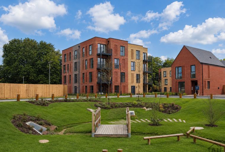 A modern housing development with apartment buildings and a house, surrounded by landscaped gardens and a children's play area.