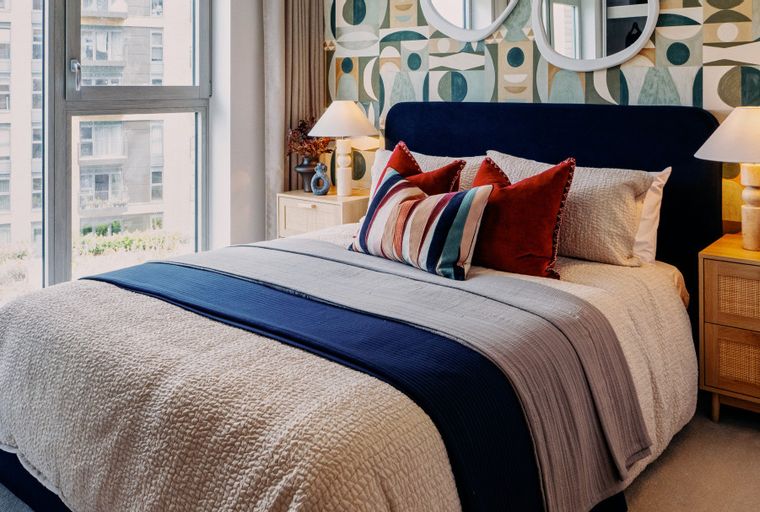 A bedroom with a bed, pillows, blankets, bedside tables, and a window.
