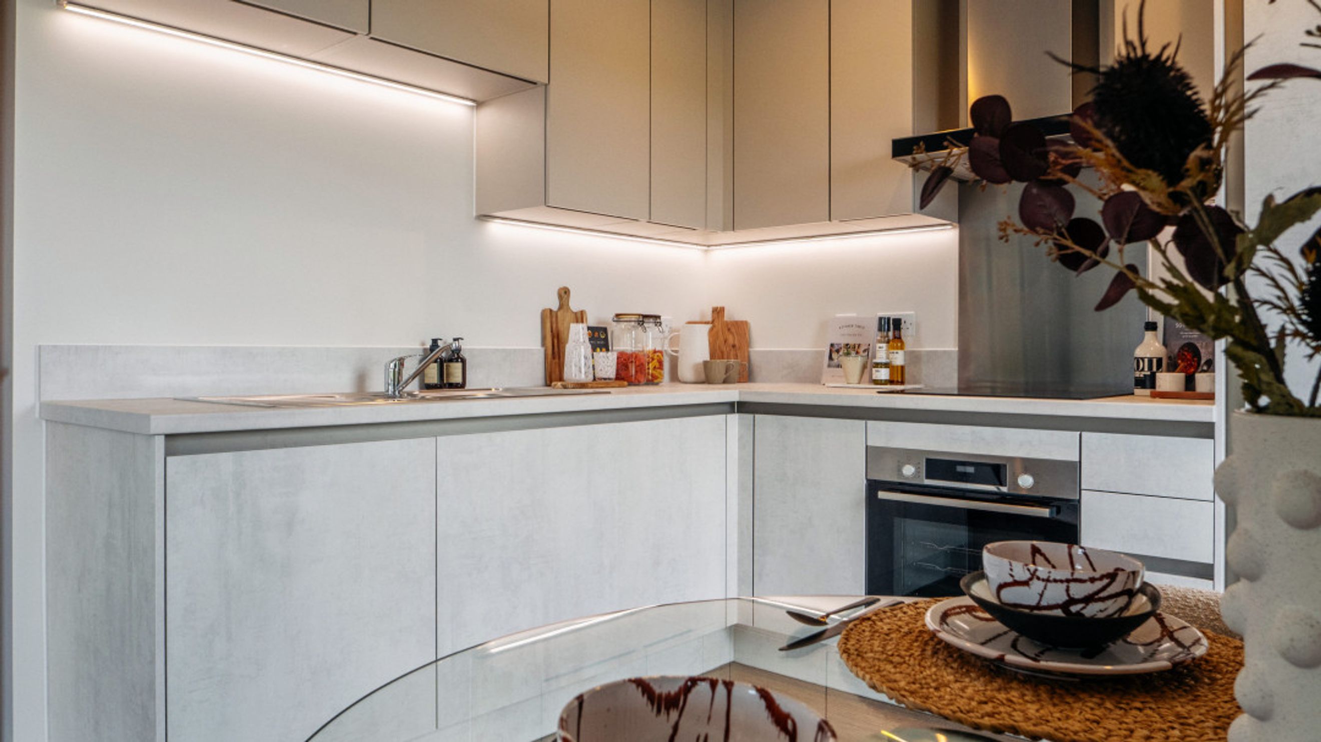 A modern kitchen with light grey cabinets, a sink, and an oven.