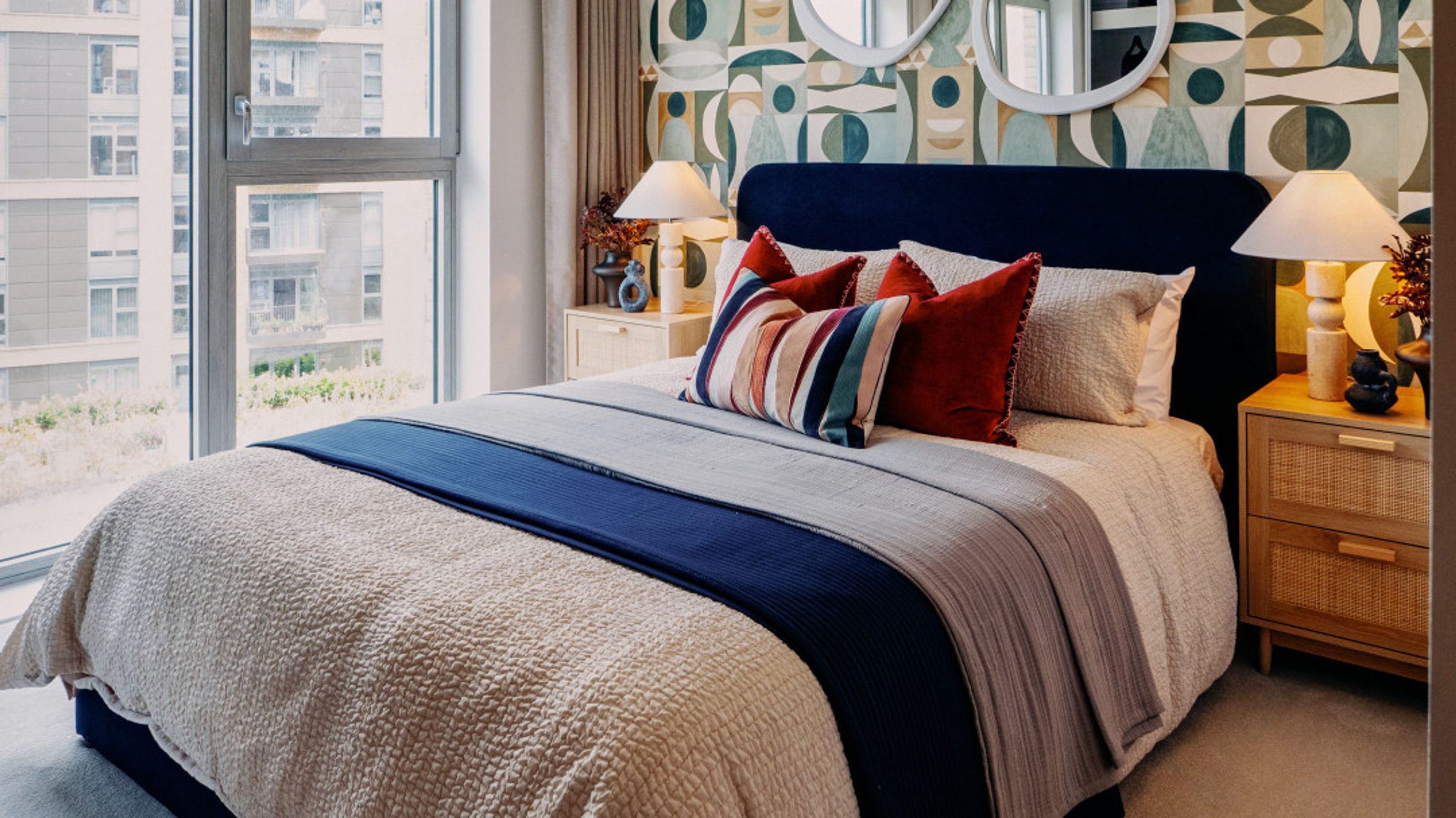 A bedroom with a bed, pillows, blankets, bedside tables, and a window.