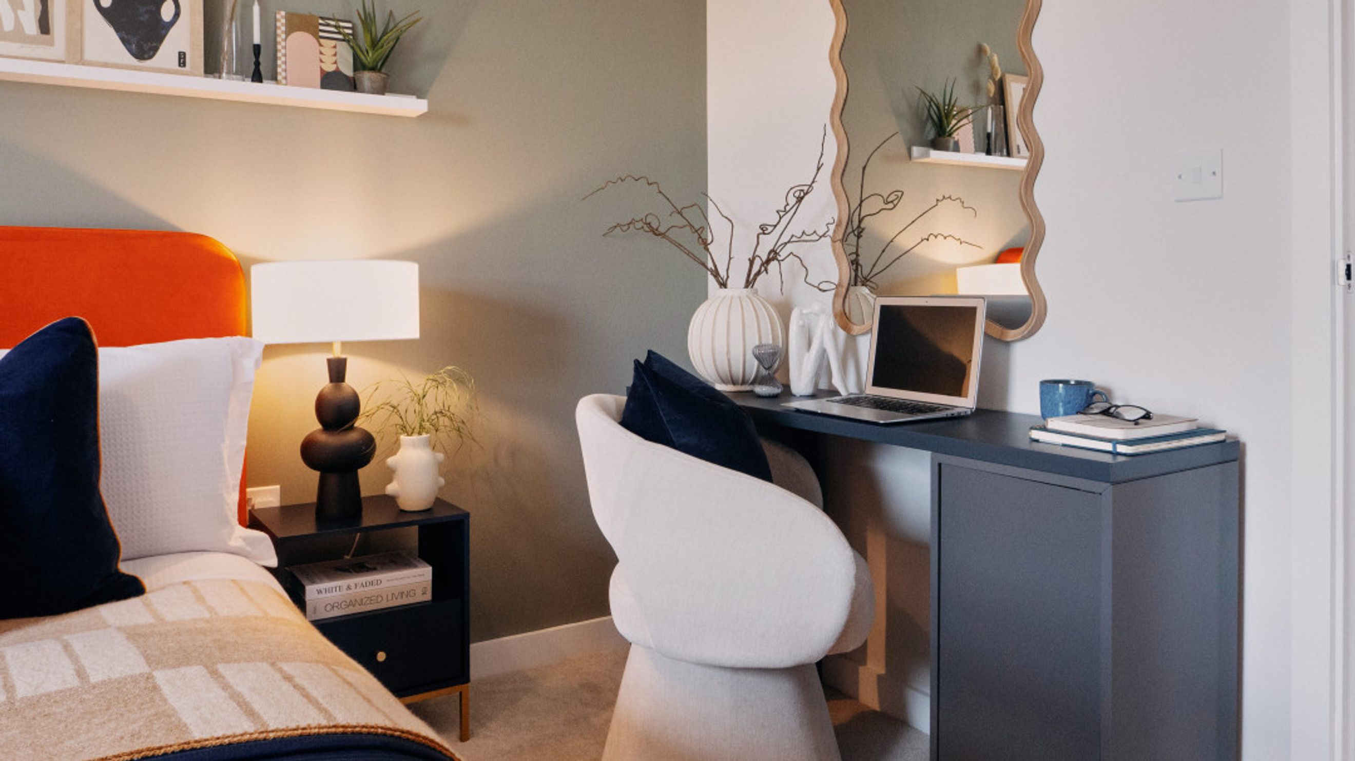 A bedroom with a bed, bedside table, desk, chair, and mirror.