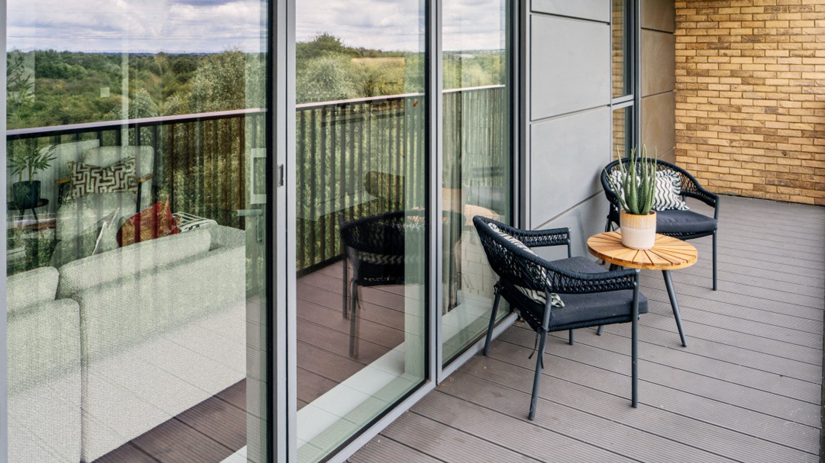 A balcony with two chairs, a table, and a plant, overlooking a wooded area.
