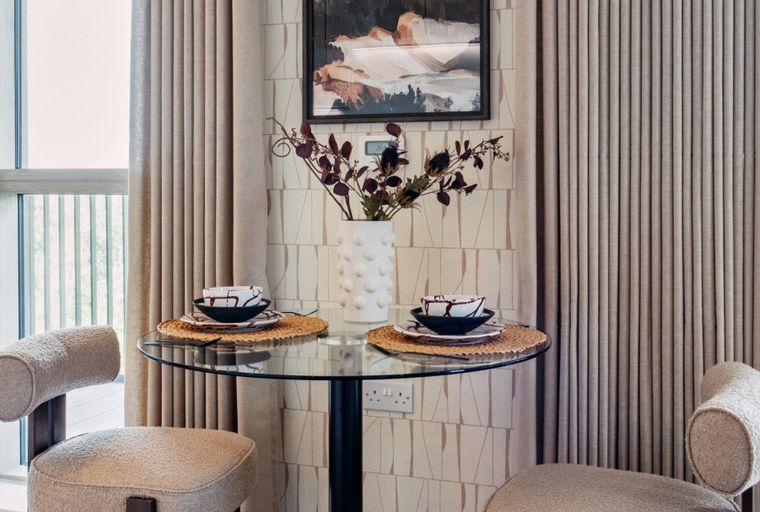 A glass-top dining table with two chairs, a vase of flowers, and a painting on the wall.