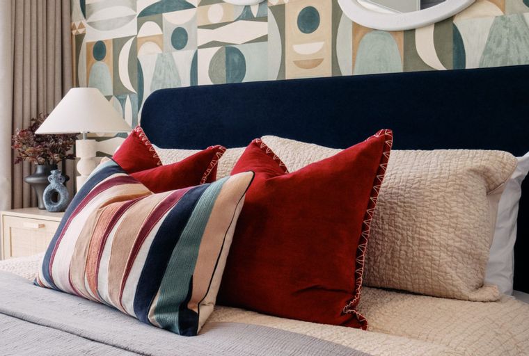 A bedroom with a bed, pillows, a headboard, a lamp, and wallpaper.