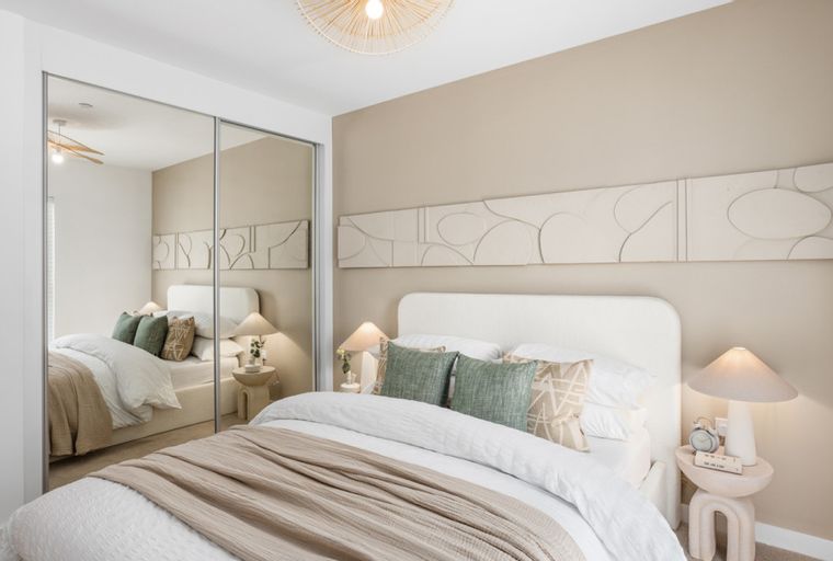 A bedroom with a bed, pillows, a throw blanket, bedside tables, lamps, and a mirrored wardrobe.