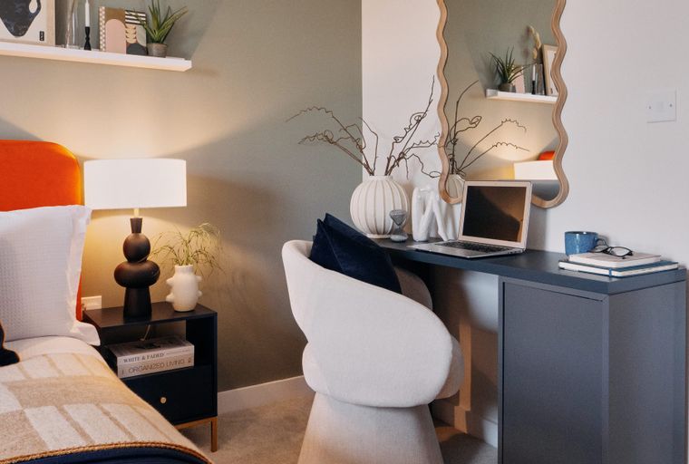 A bedroom with a bed, bedside table, desk, chair, and mirror.