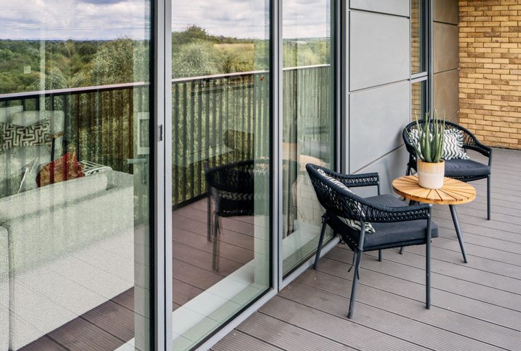 A balcony with two chairs, a table, and a plant, overlooking a wooded area.