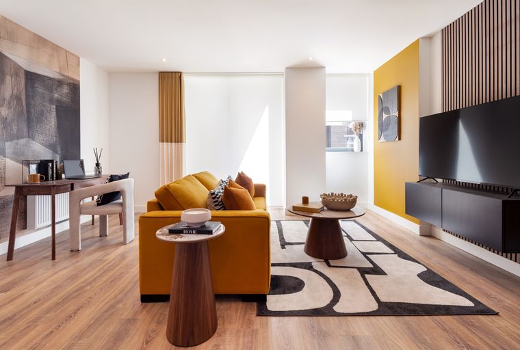 A living room with an orange sofa, coffee tables, a television, and a desk.