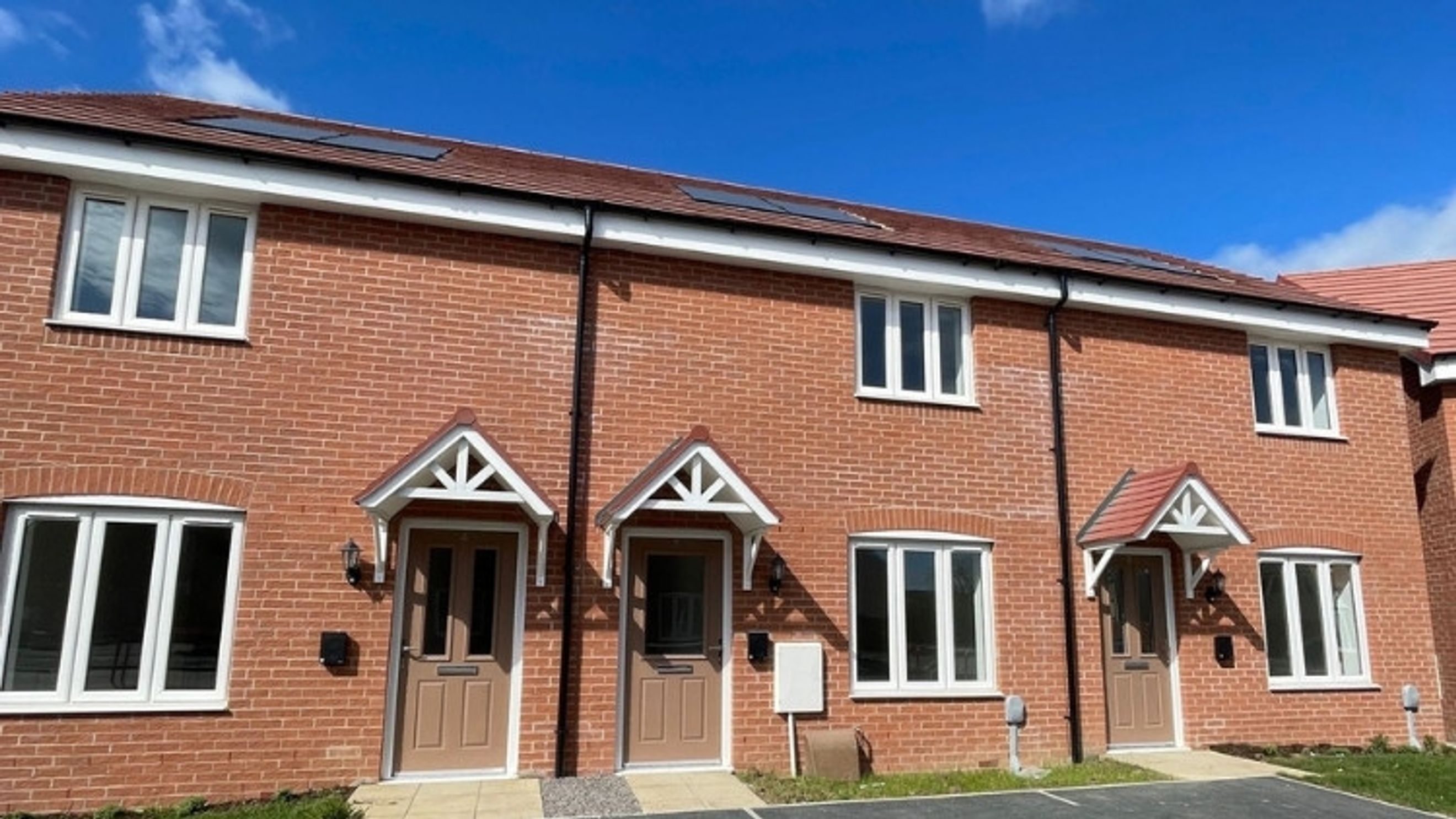 A row of brick townhouses with white-framed windows and brown front doors under a blue sky.