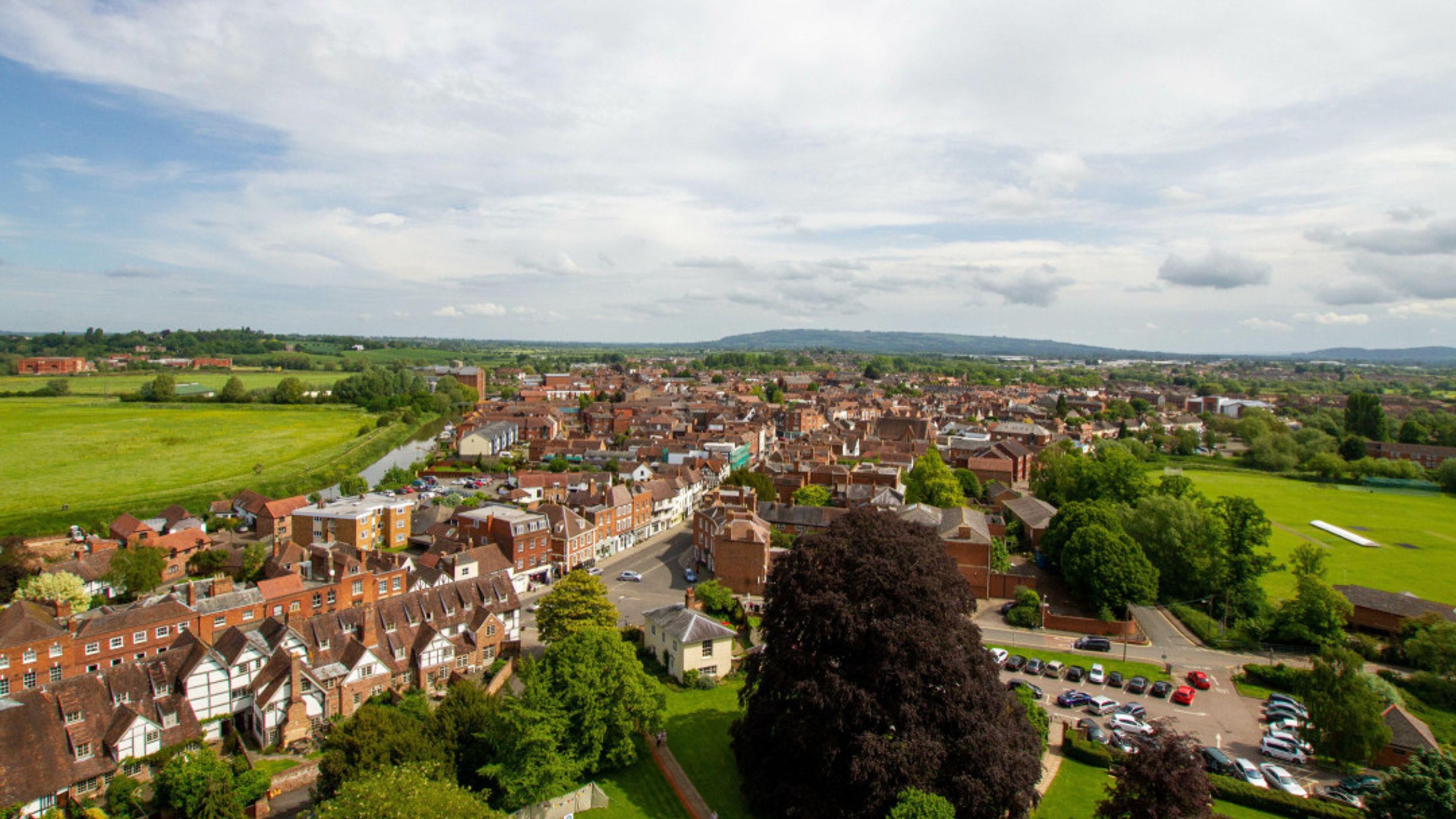 An aerial view of a town with red-tiled roofs, green fields, and a canal.