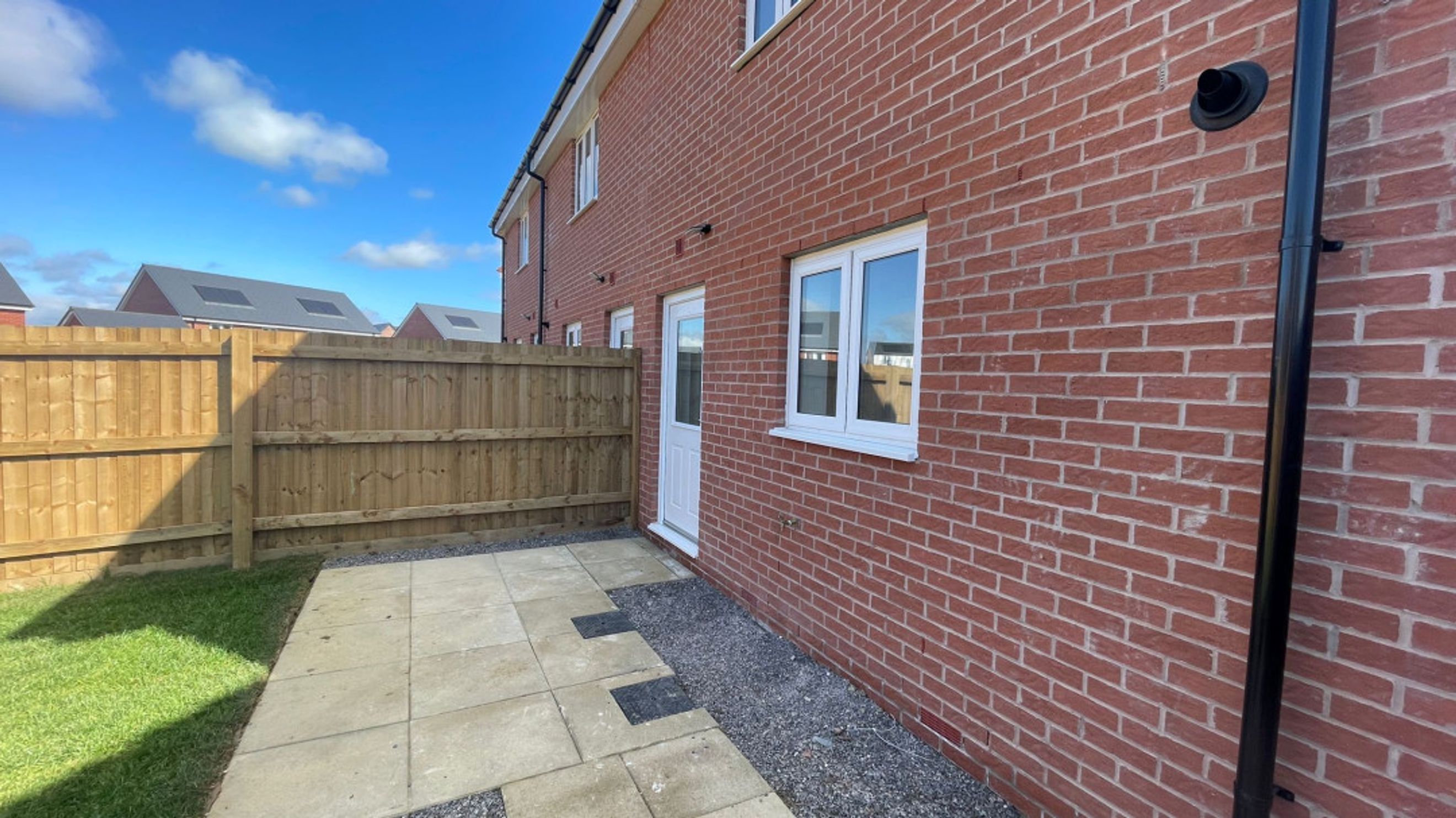 A backyard with a paved patio, a wooden fence, and a brick house.