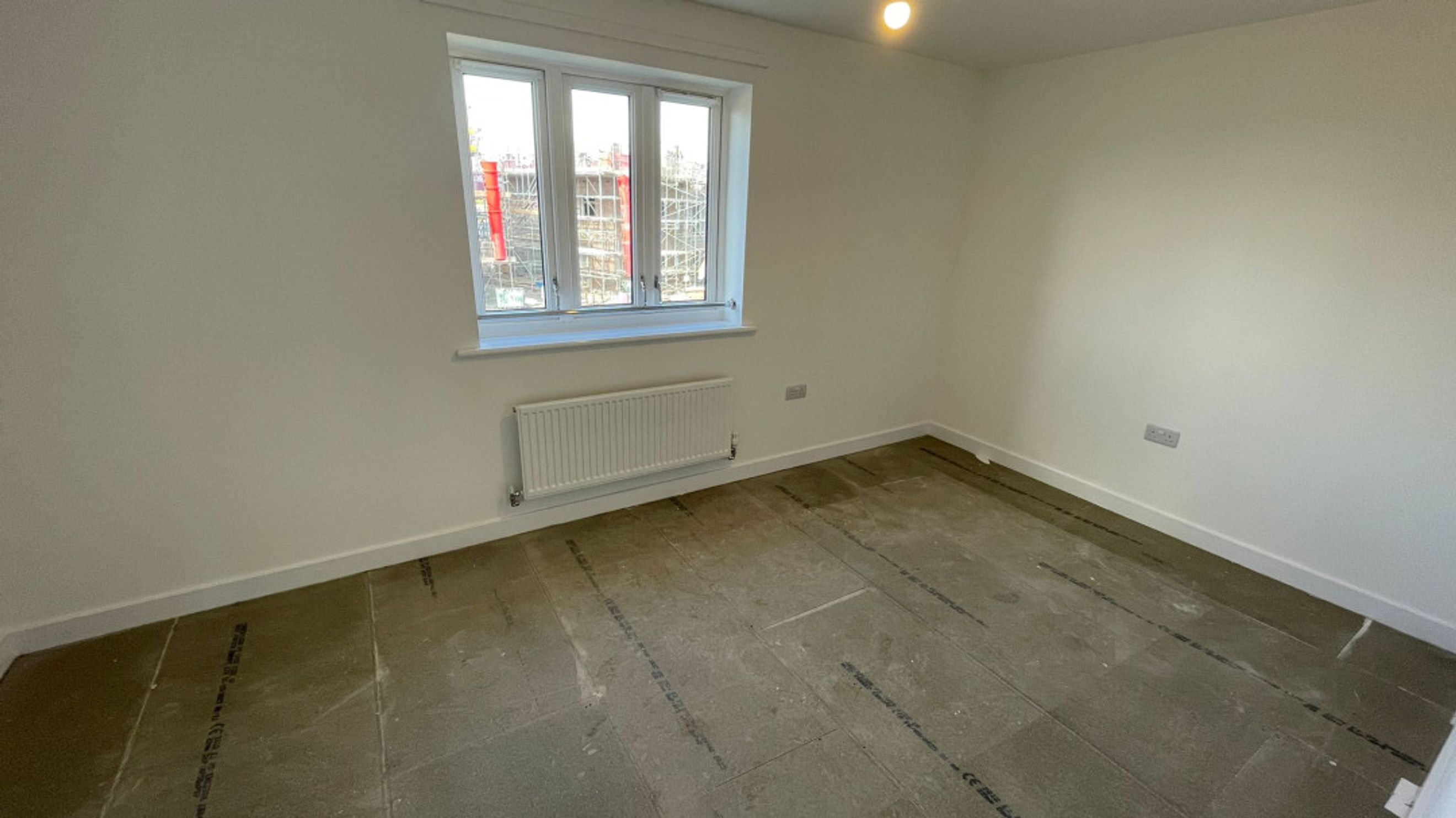 A room with a window, radiator, and unfinished floor.