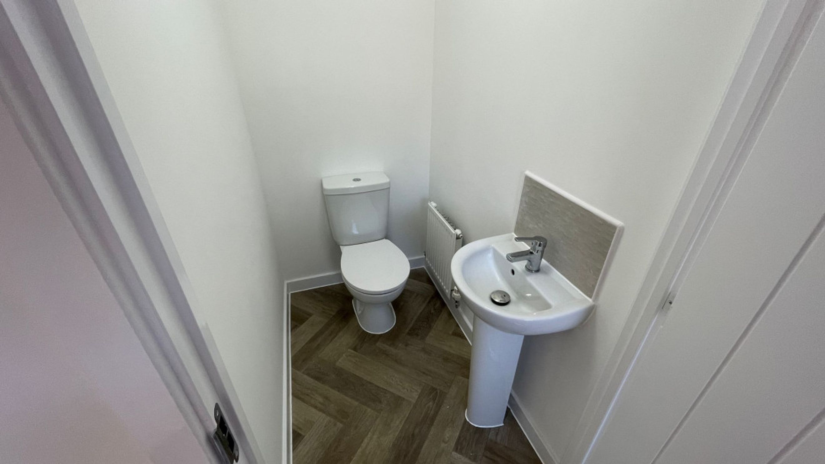 A toilet and a sink in a bathroom with herringbone flooring.