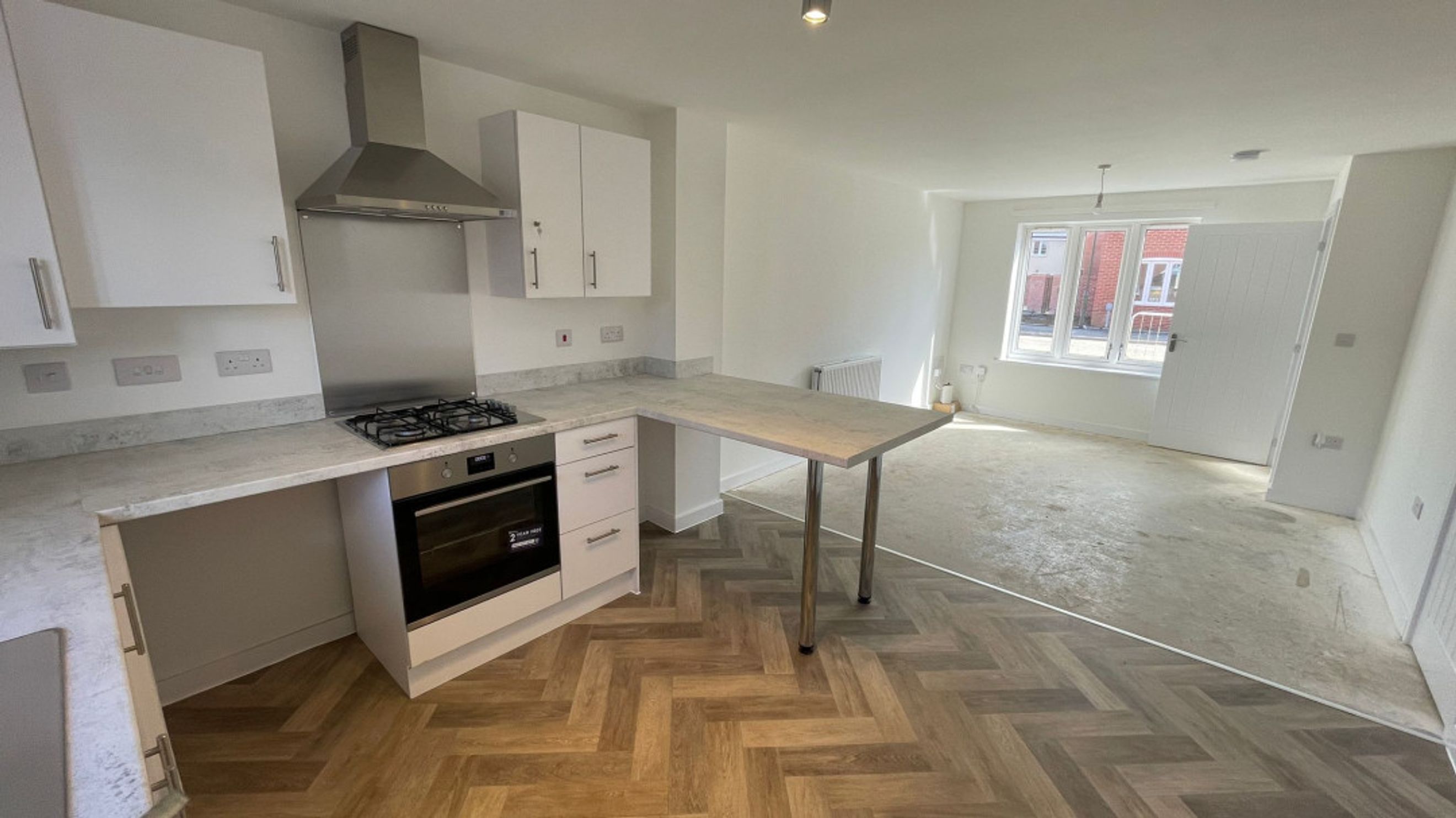 A kitchen and living area with white cabinets, a gas hob, an oven, and a breakfast bar.