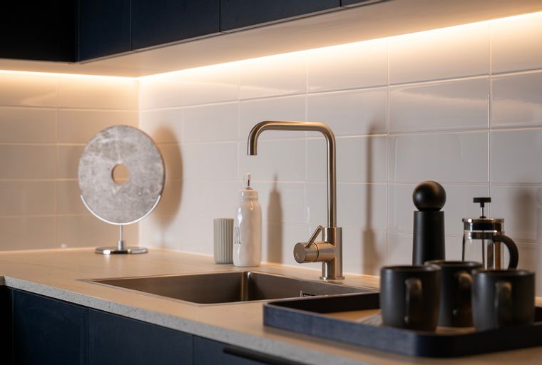 A kitchen sink with a faucet, soap dispenser, and mugs on a tray.