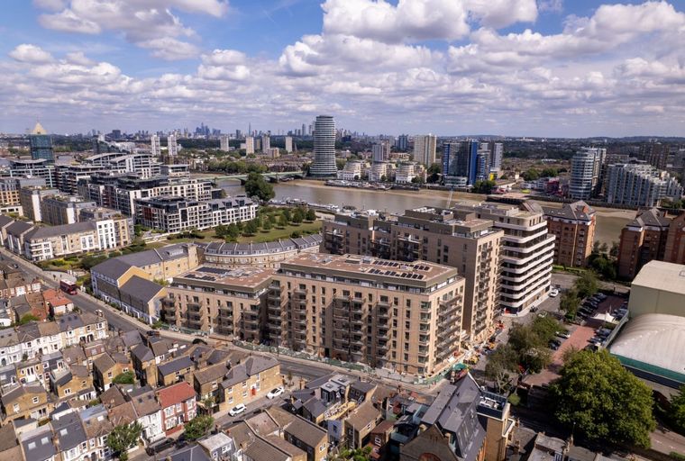 An aerial view of a modern apartment complex situated along a river, with a cityscape in the background.