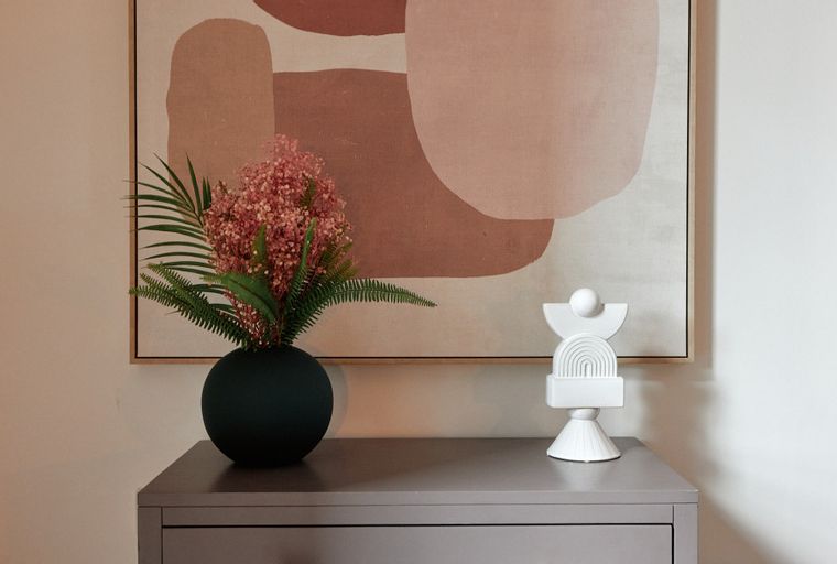 A console table with a vase of flowers and a sculpture in front of a painting.