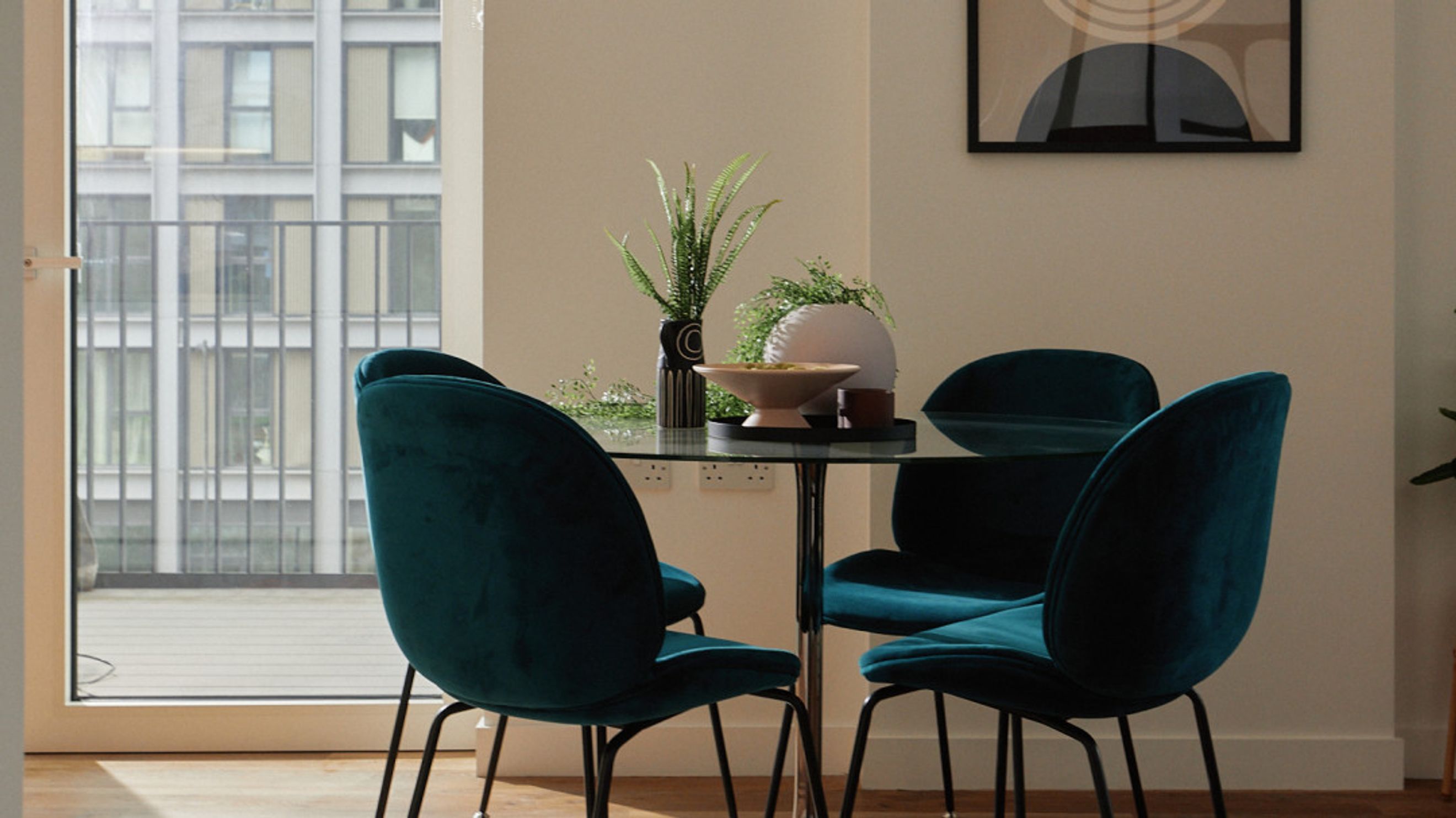 A dining set with four teal velvet chairs and a glass-top table.