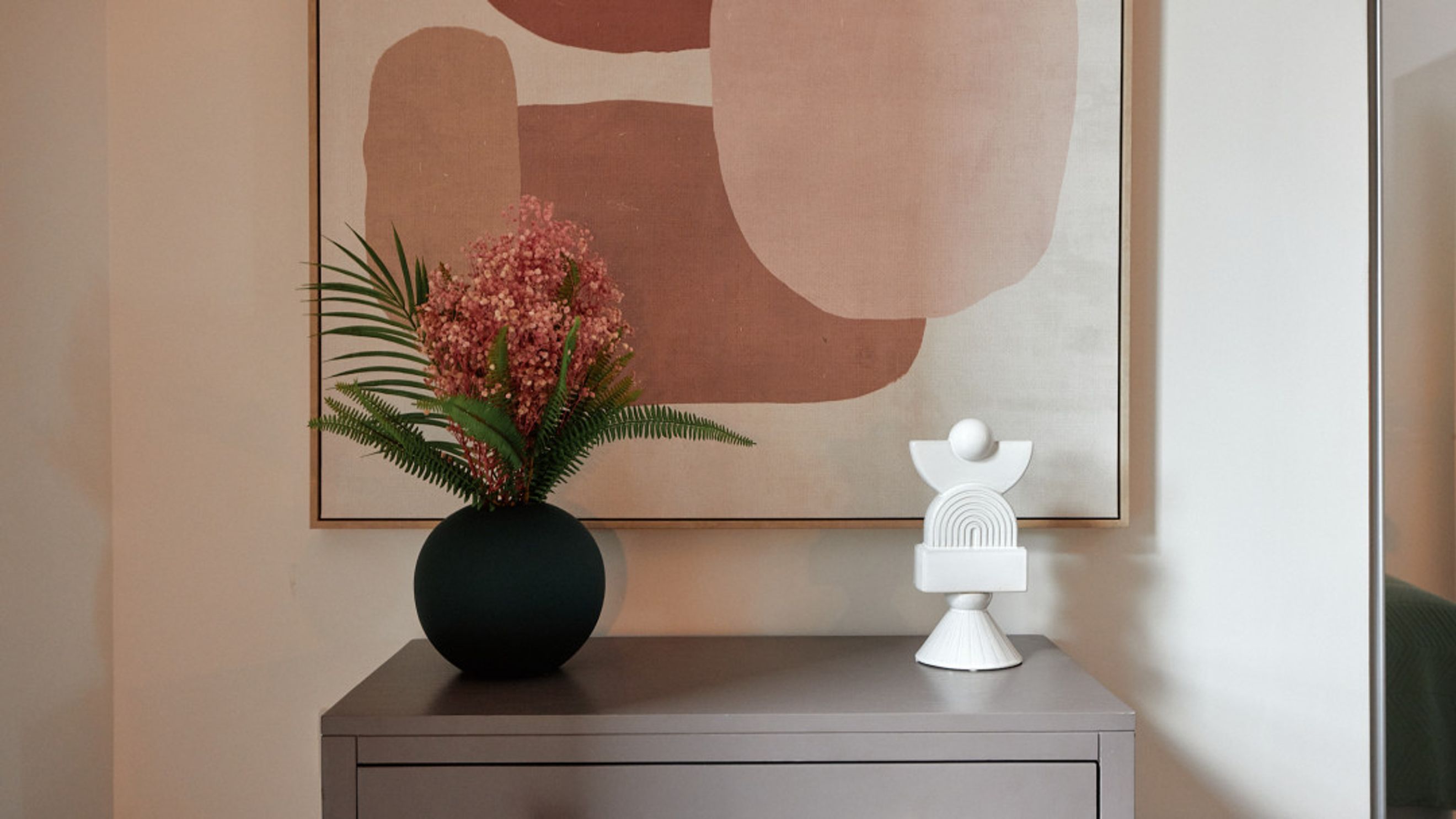 A console table with a vase of flowers and a sculpture in front of a painting.