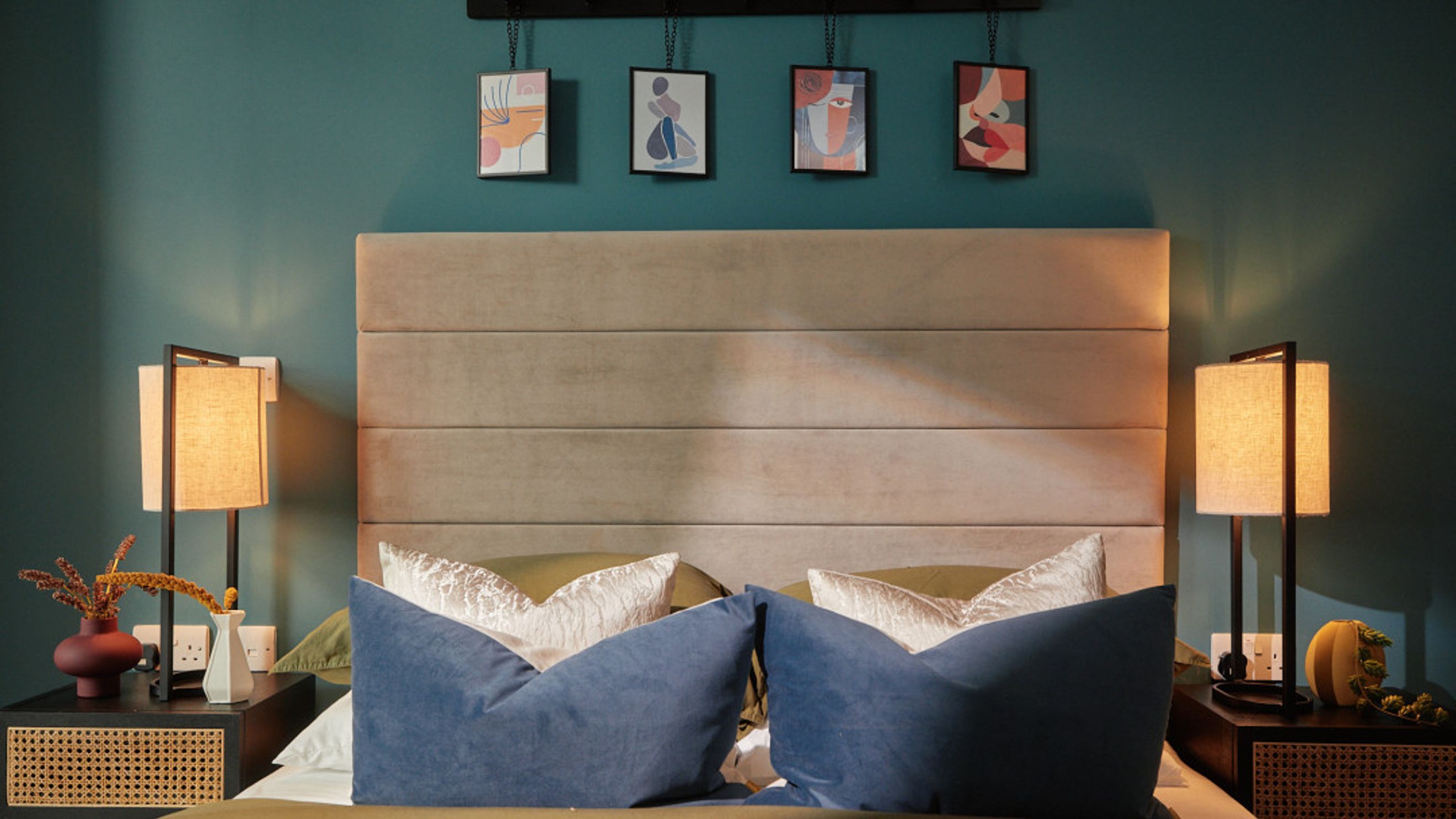 A bedroom with a bed, headboard, bedside tables, lamps, and artwork.