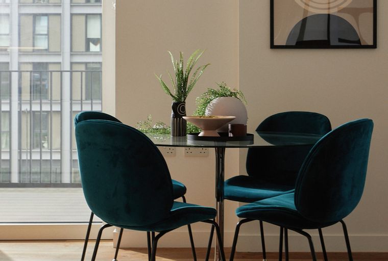 A dining set with four teal velvet chairs and a glass-top table.