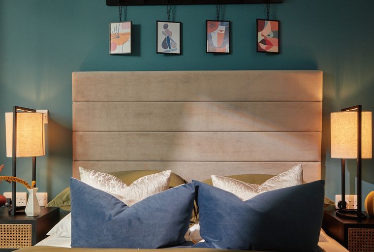A bedroom with a bed, headboard, bedside tables, lamps, and artwork.