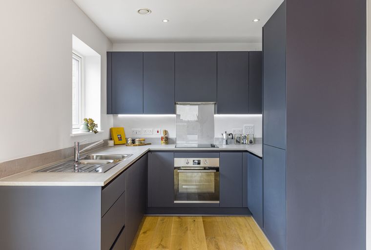 A modern kitchen with dark grey cabinets, a stainless steel sink, and an integrated oven.