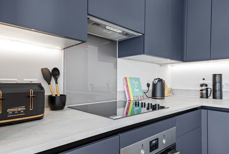 A modern kitchen with dark blue cabinets, a concrete countertop, an induction hob, and an oven.