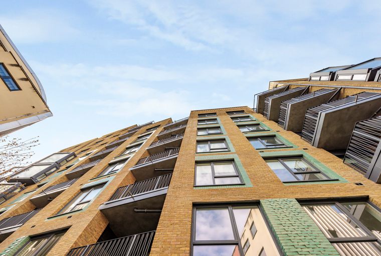 A modern apartment building with yellow brick and green tile accents, viewed from a low angle against a blue sky.