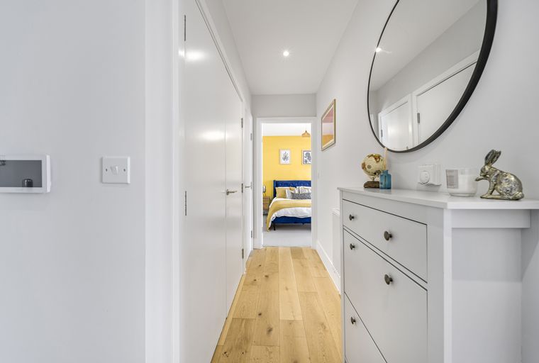 A hallway with a chest of drawers and a mirror, leading to a bedroom with a yellow wall and a blue bed.