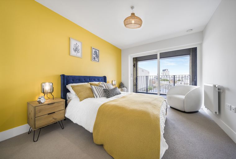 A bedroom with a bed, nightstand, armchair, and a balcony.