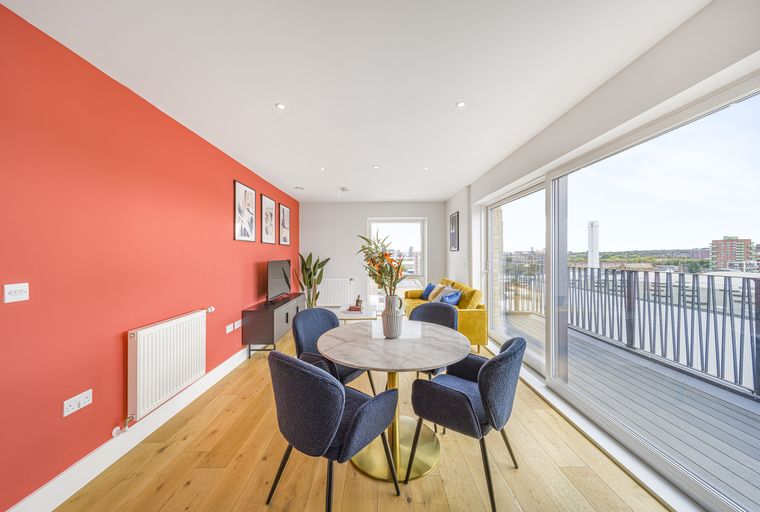 A dining area with a marble table and chairs next to a yellow sofa and a large window overlooking a city view.