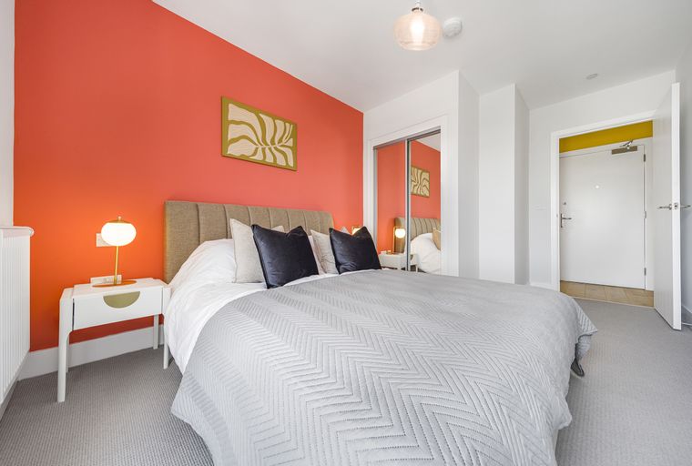 A bedroom with a bed, nightstand, and a coral accent wall.
