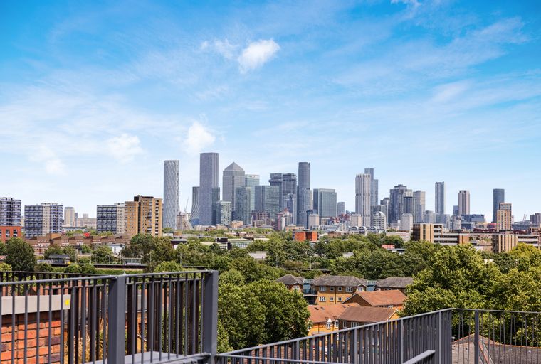 A cityscape with modern skyscrapers and residential buildings, seen from a balcony with a railing.