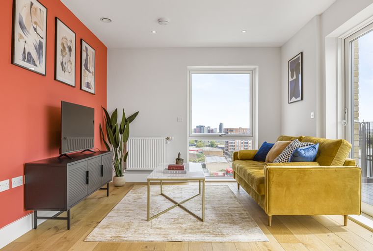 A living room with a yellow sofa, coffee table, and a TV stand against a coral wall.