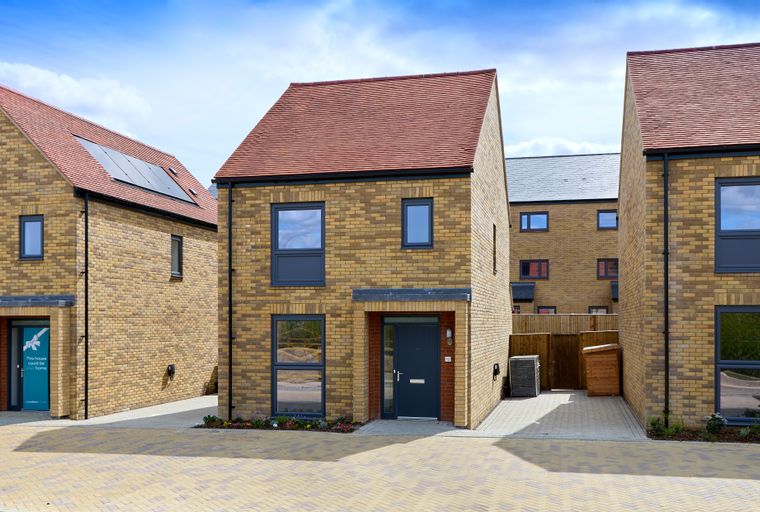 A row of modern brick houses with red tiled roofs and dark windows under a blue sky.