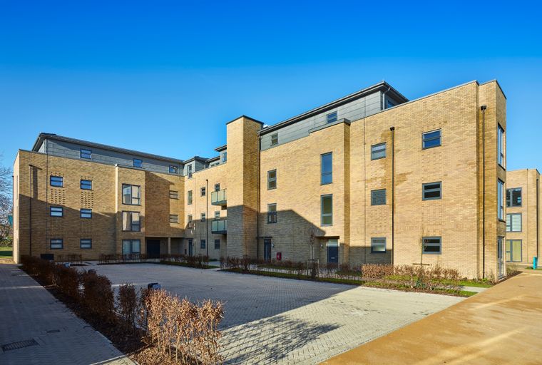 A modern apartment building with brick exterior and balconies under a clear blue sky.