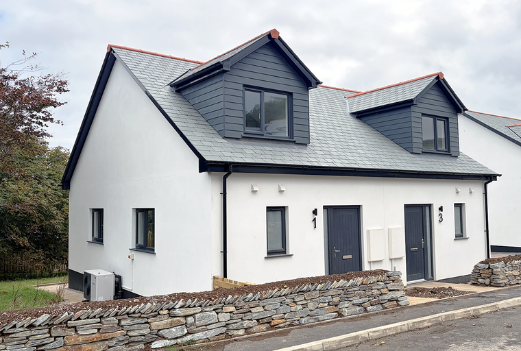 A row of modern white houses with dark grey dormer windows and slate roofs.
