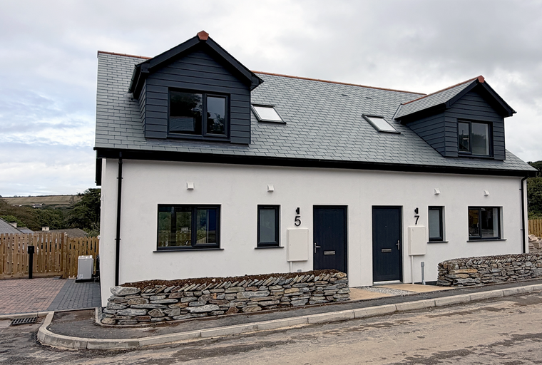 A modern duplex with white walls, dark dormers, and slate roofs.