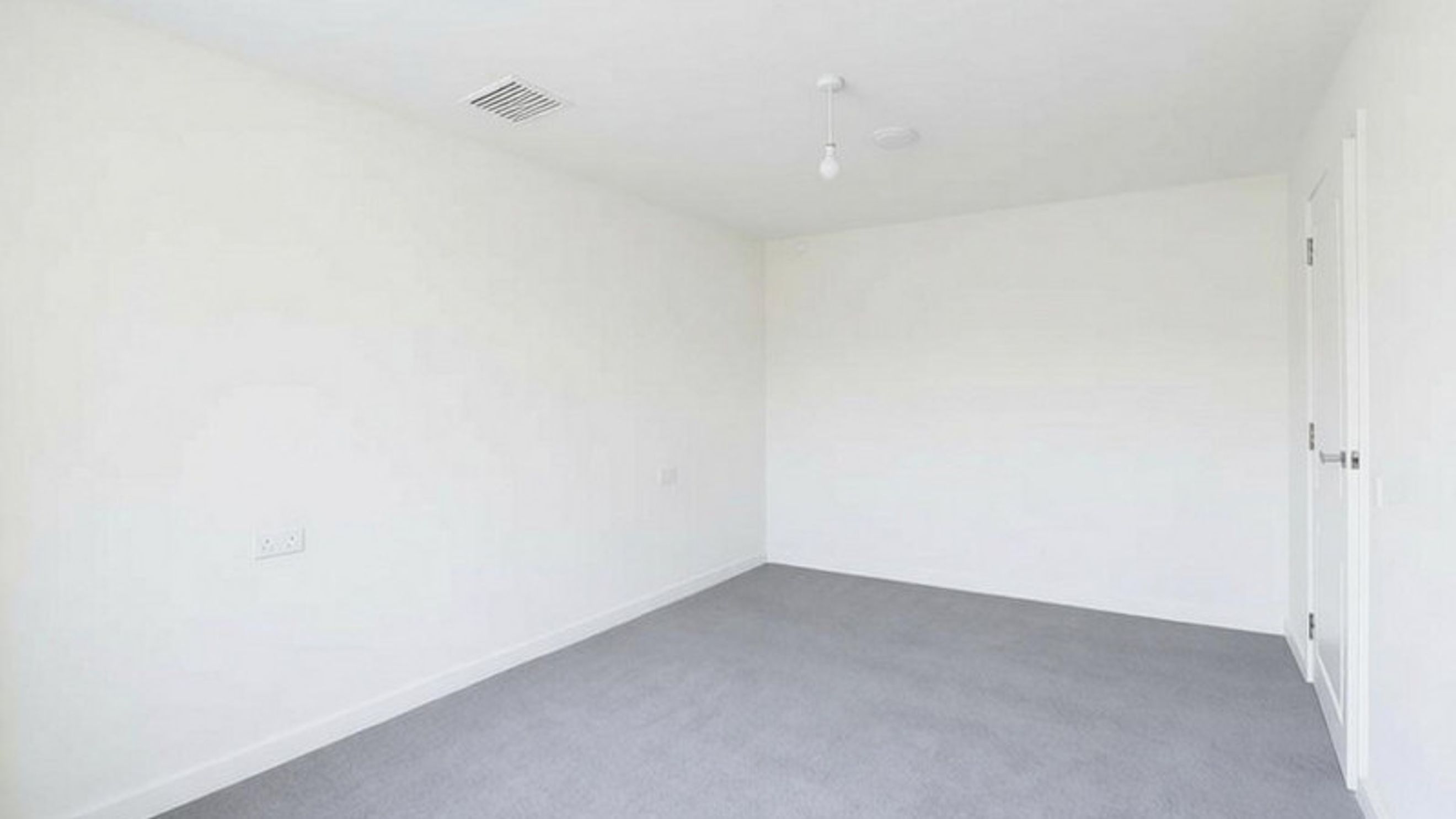 A room with white walls, gray carpet, a light fixture, and a door.