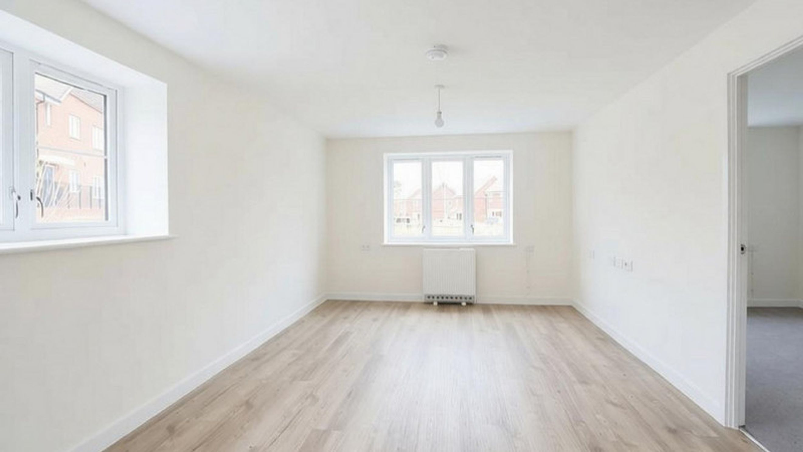 A bright, empty room with light wood laminate flooring and two windows.